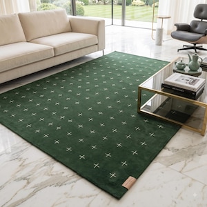 Puede incluir: Una alfombra rectangular de color verde bosque profundo con un patrón repetitivo de pequeños símbolos blancos en forma de cruz. La alfombra tiene una textura lisa de pelo corto e incluye una pequeña etiqueta de marca rectangular de color beige.