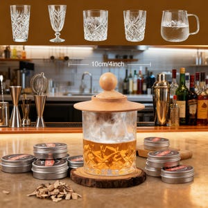 Pode incluir: Uma composição de copos de cristal, incluindo copos altos e uma caneca com alça. Um grande recipiente de vidro com tampa e base de madeira está no centro, juntamente com pequenas latas de metal. A imagem inclui uma régua de 10 cm.