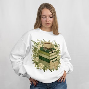 May include: White sweatshirt with a design of green books, a coffee cup, and spectacles. The illustration includes a floral arrangement with white roses and a bow. The theme is a cosy, book-loving aesthetic.