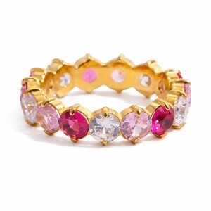 May include: A gold-toned ring featuring a series of alternating pink, white, and fuchsia-colored gemstones. The gemstones are oval-shaped and set in a continuous band around the ring.