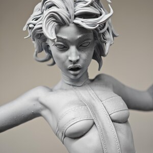 May include: A grey sculpture of a woman with intricate, swirling hair. The figure is posed with one arm extended, wearing a detailed bodice and a strap down the centre. The sculpture has a detailed face with an open mouth.