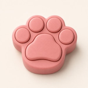 May include: A solid, dusty rose-coloured object shaped like an animal paw print. The design features four circular toe pads arranged in an arc above a single, larger, central pad shaped like a heart or a rounded triangle, all with a smooth finish.
