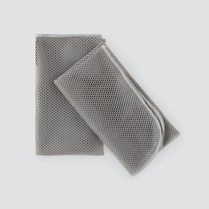 May include: Two gray mesh laundry bags, one folded and the other open, are displayed against a white background. The bags have a fine, perforated texture and a simple, minimalist design, suitable for delicate items.