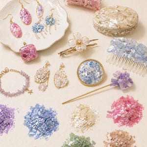 May include: An assortment of iridescent jewelry and hair accessories in shades of pink, blue, and white. The collection includes earrings, bracelets, hair clips, and a decorative box, all featuring a shimmering, shell-like texture.
