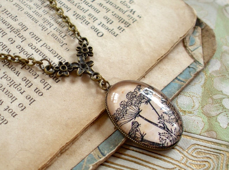 May include: A bronze necklace with a delicate floral design and a pendant featuring a vintage botanical illustration of Queen Anne's Lace on a cream background.