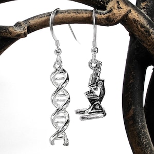 May include: A pair of silver earrings with a DNA helix and a microscope pendant. The earrings are hanging from a branch.