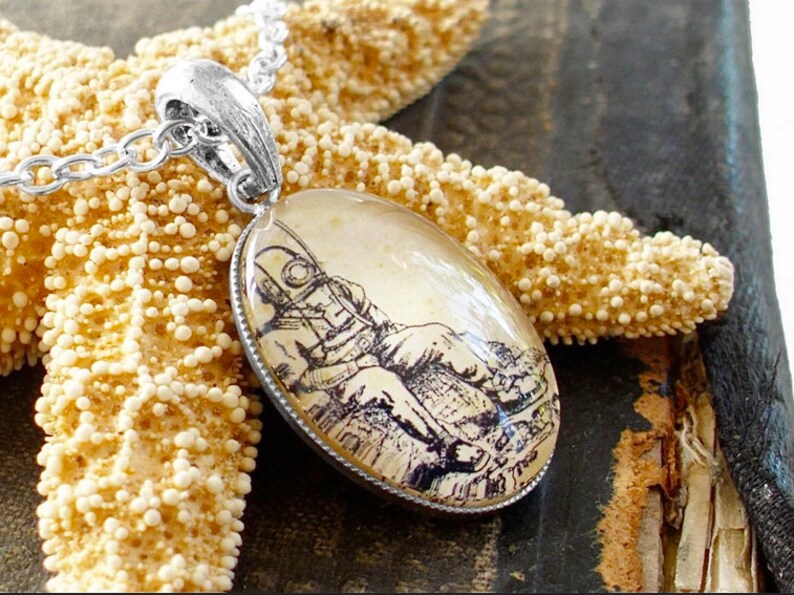 Op de afbeelding: Een zilveren ketting met een ronde hanger met een vintage illustratie van een duiker in een duikpak. De hanger is geplaatst op een beige achtergrond en heeft een zilveren rand.