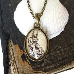 Op de afbeelding: Een bronzen ketting met een glazen hanger met een vintage illustratie van een duiker in een duikpak. De hanger is rond en heeft een transparante glazen achtergrond.