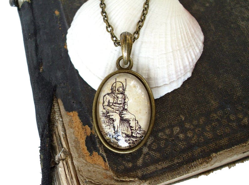 Op de afbeelding: Een bronzen ketting met een glazen hanger met een vintage illustratie van een duiker in een duikpak. De hanger is rond en heeft een transparante glazen achtergrond.