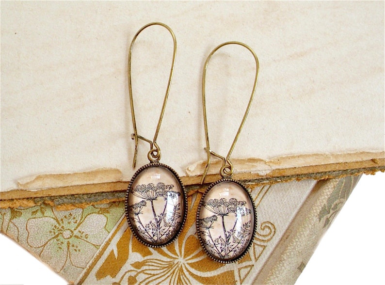 May include: A pair of bronze dangle earrings with oval-shaped glass charms featuring a vintage botanical print of delicate flower sprigs.