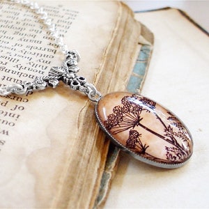 May include: A silver chain necklace with a floral design pendant. The pendant features a glass oval with a black and white image of a flower.