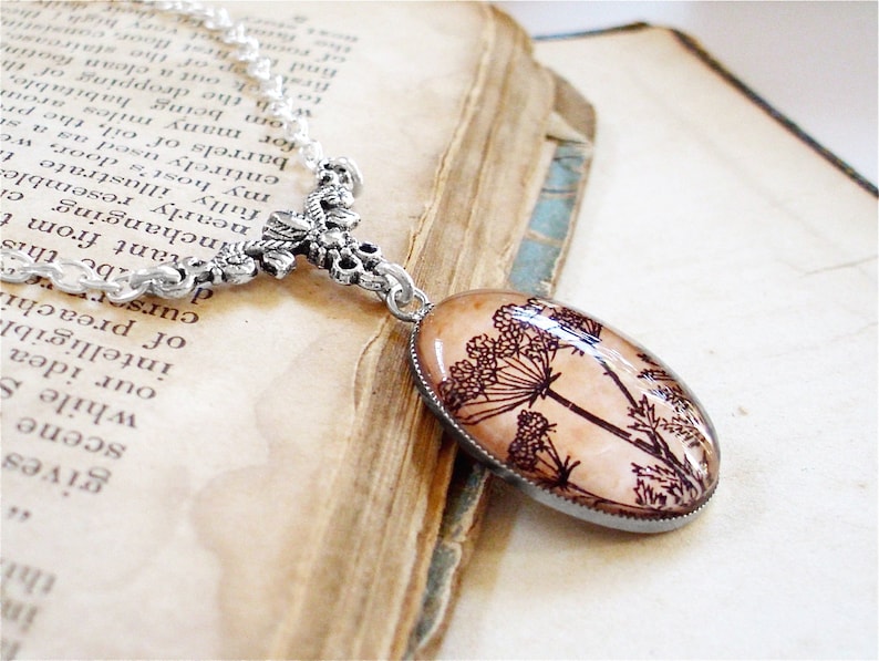 May include: A silver chain necklace with a floral design pendant. The pendant features a glass oval with a black and white image of a flower.