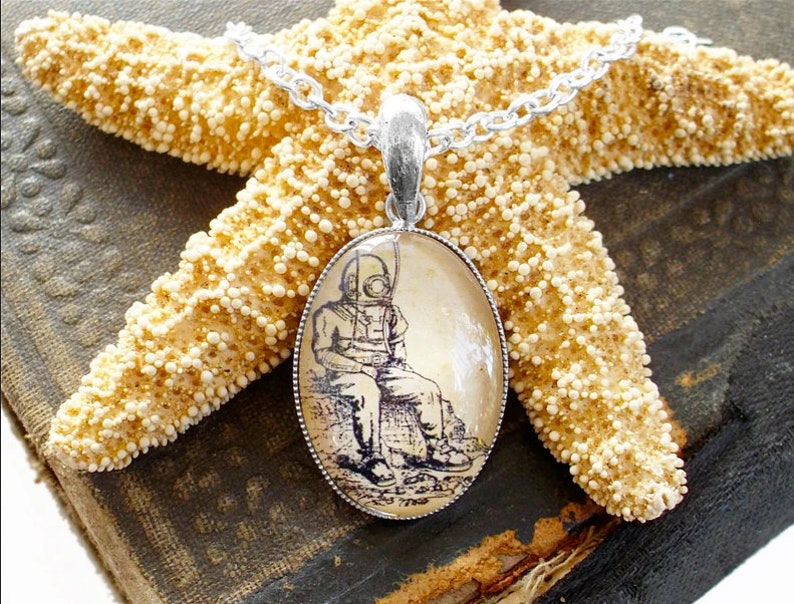 Op de afbeelding: Een zilveren ketting met een ronde hanger met een vintage illustratie van een duiker in een duikpak. De hanger is geplaatst in een transparante glazen koepel.