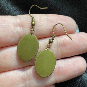 May include: A pair of oval-shaped earrings with a gold finish and a simple hook closure.