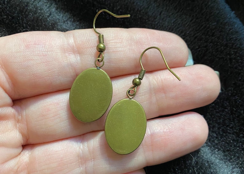 May include: A pair of oval-shaped earrings with a gold finish and a simple hook closure.