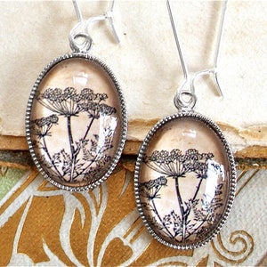 May include: A pair of silver earrings with a delicate floral design. The earrings feature a clear glass oval with a black and white image of a flower.