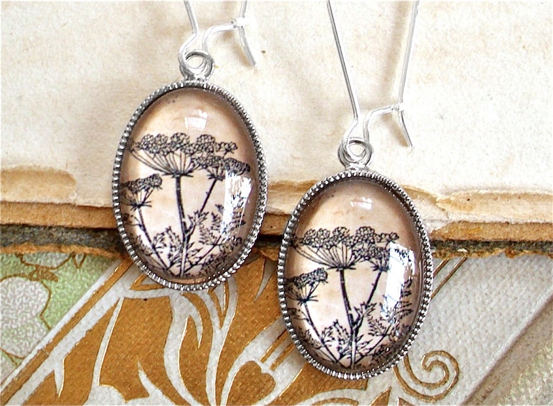 May include: A pair of silver earrings with a delicate floral design. The earrings feature a clear glass oval with a black and white image of a flower.