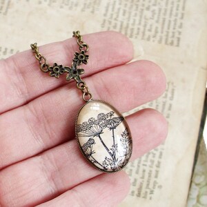 May include: A delicate bronze necklace with a floral design and a pendant featuring a pressed flower image. The pendant is oval-shaped and has a clear glass cover.