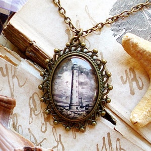 Op de afbeelding: Een bronzen ketting met een hanger met een glazen cameo met een zwart-wit afbeelding van een vuurtoren. De cameo is ingelijst in een decoratief frame met een filigraan ontwerp.