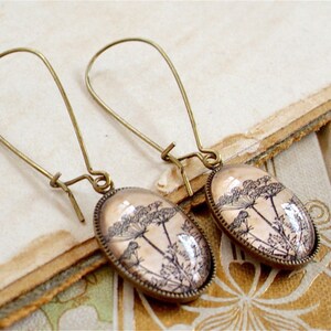 May include: A pair of bronze dangle earrings with oval-shaped glass pendants featuring a delicate black and white botanical illustration of a flower.