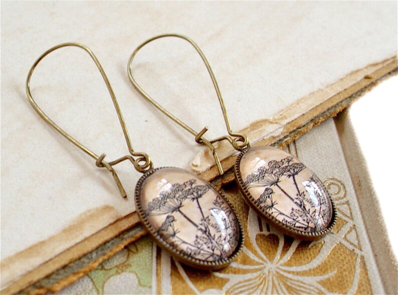 May include: A pair of bronze dangle earrings with oval-shaped glass pendants featuring a delicate black and white botanical illustration of a flower.