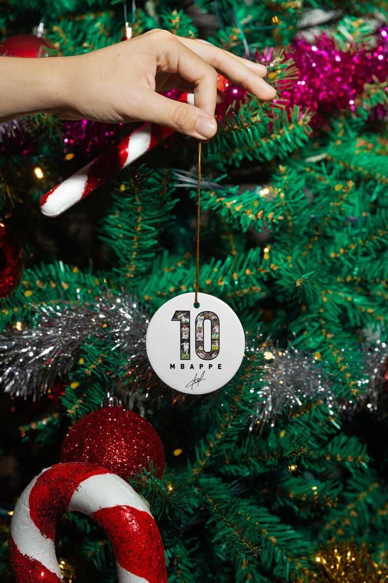 A hand is holding a white ornament with the number 10 on it, hanging from a Christmas tree decorated with red and white ornaments, tinsel, and other festive decorations.