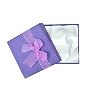 An open purple gift box with a pink bow, revealing a white interior.
