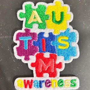May include: A colourful patch in the shape of a jigsaw puzzle, with the word "AUTISM" spelled out in individual puzzle pieces. The word "awareness" is written below. The patch features green, yellow, purple, blue, and red colours.