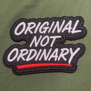 May include: A black embroidered patch with a scalloped border featuring the white text ORIGINAL NOT ORDINARY in a bold, sans-serif font, with a thin horizontal red line positioned directly underneath the word ORDINARY.