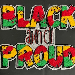 May include: Embroidered patch with the words "BLACK and PROUD" in bold, colorful letters. The letters are filled with red, yellow, and green patterns, outlined in silver, and set against a black background.