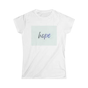 Könnte beinhalten: Weißes T-Shirt mit einem hellblauen Rechteck auf der Vorderseite. Das Wort "hope" ist in einer Schreibschrift in der Mitte des Rechtecks geschrieben. Das Wort ist schwarz mit einem blauen Farbverlauf.