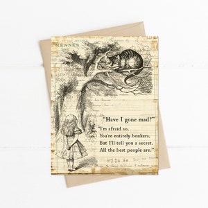 May include: A vintage-style greeting card featuring an illustration from Alice in Wonderland. The black and white image shows Alice, the Cheshire Cat in a tree, and text from the story. The card is on a beige envelope.