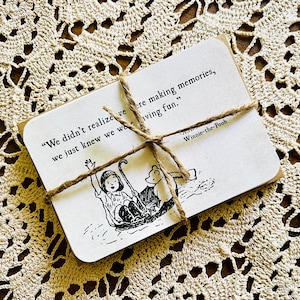 May include: A Winnie-the-Pooh quote card with a black and white illustration of Winnie-the-Pooh and Piglet on a boat. The quote reads, "We didn't realize we were making memories, we just knew we were having fun."