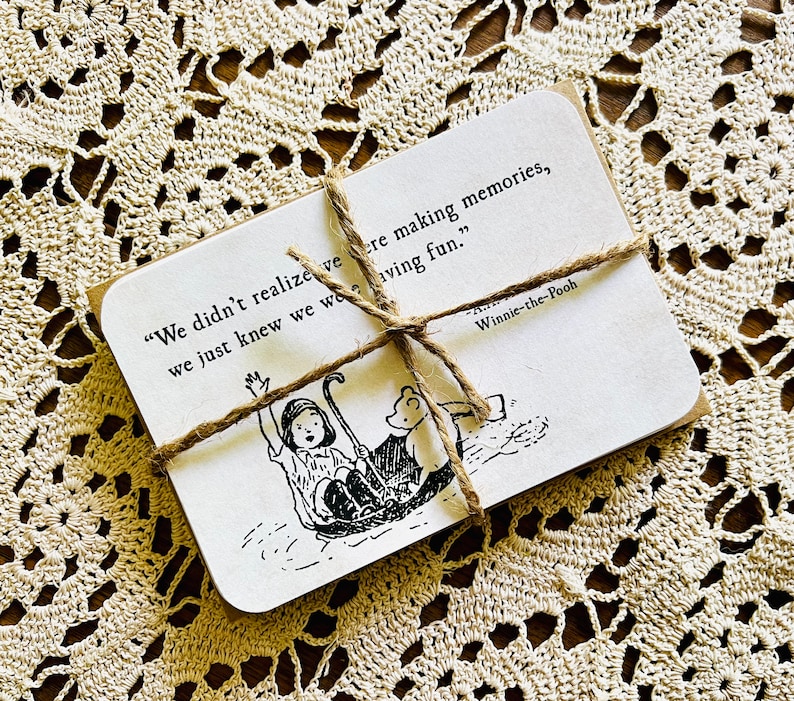May include: A Winnie-the-Pooh quote card with a black and white illustration of Winnie-the-Pooh and Piglet on a boat. The quote reads, "We didn't realize we were making memories, we just knew we were having fun."