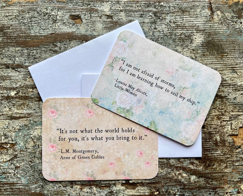 Może przedstawiać: Dwie karty z nadrukowanymi inspirującymi cytatami. G&oacute;rna karta zawiera cytat z "Małych kobiet" autorstwa Louisa May Alcott, a dolna karta zawiera cytat z "Anny z Zielonego Wzg&oacute;rza" autorstwa L.M. Montgomery. Obie karty mają kwiatowy wz&oacute;r.