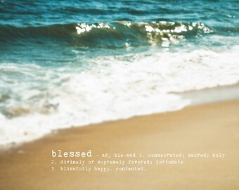 May include: A blurry image of a sandy beach with a wave crashing on the shore. The word "blessed" is written in white text on the sand with a definition below it.