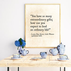 May include: A framed print with a quote from Louisa May Alcott's "Little Women" that reads, "You have so many extraordinary gifts; how can you expect to lead an ordinary life?" The quote is printed in black text on a cream background. The print is sitting on a wooden table with blue and white teacups and a bouquet of blue hydrangeas.