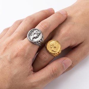 May include: Two rings, one silver and one gold, each featuring a coin design with a profile of a person. The silver ring has the word "CAESAR" on it. The gold ring has a textured band.