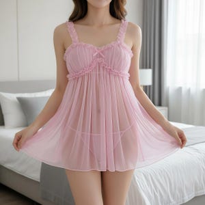 Könnte beinhalten: Hellrosa Babydoll-Dessous-Set. Der transparente Stoff hat Rüschenbesatz am Ausschnitt und an den Trägern, mit einer kleinen Schleife an der Brust. Das Set enthält einen passenden String.