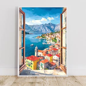 May include: A framed watercolor painting depicts a coastal town scene viewed through an open window. The artwork showcases a vibrant blue sea, a town with red-roofed buildings, and distant mountains under a bright blue sky. The window frame is brown.