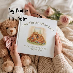 May include: A white hardcover book titled Our Forest Adventure with an illustration of two teddy bears under a patchwork quilt. The text reads To The Newest Big Brother William Rhys. A brown teddy bear with a pink satin bow sits beside the book.