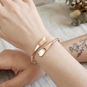 May include: A rose gold cuff bracelet with a hammered texture. The open design features two teardrop-shaped ends that gently curve around the wrist. Jewelry for everyday wear.