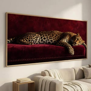 Puede incluir: Una impresión de arte mural rectangular que muestra a un leopardo con pelaje manchado descansando sobre una superficie de terciopelo rojo intenso. El leopardo está colocado horizontalmente, con la cabeza gacha y una pata delantera colgando.