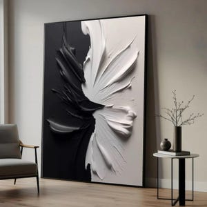 Può includere: Grande opera d'arte astratta in bianco e nero. L'opera è divisa verticalmente, con un lato nero e l'altro bianco. La vernice strutturata crea un design dinamico, a forma di fiore. L'opera è incorniciata in nero e appoggiata a un muro.