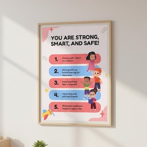 Könnte beinhalten: Ein gerahmtes Poster mit dem Text "YOU ARE STRONG, SMART, AND SAFE!" und fünf illustrierten Regeln für Kinder. Das Poster zeigt farbenfrohe Grafiken von Kindern und Regenbögen mit einem hellen Holzrahmen.