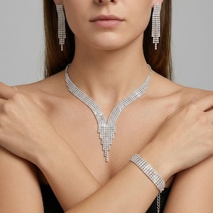 May include: A glamorous jewellery set comprising a necklace, bracelet, and earrings. The necklace and earrings have a cascading design, while the bracelet is a simple band. All pieces are silver-toned and embellished with sparkling crystals, ideal for special events.