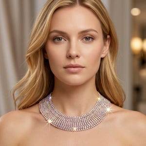 Könnte beinhalten: Eine mehrreihige Choker-Halskette mit zahlreichen Reihen kleiner, klarer, facettierter Kristalle, die das Licht einfangen. Die Kette liegt eng am Halsansatz an und bildet ein breites, schimmerndes Band aus brillant reflektierenden Steinen.