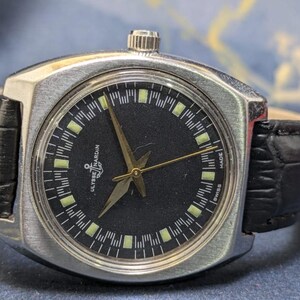May include: A vintage Ulysse Nardin wristwatch with a black dial and silver-tone case. The watch features gold hands and markers, a black leather band, and the text "Ulysse Nardin" and "Swiss Made".