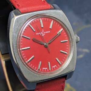 May include: A vintage wristwatch with a square silver case and a vibrant red dial. The watch features silver hands and markers, a red leather strap, and the brand name "Ulysse Nardin". The watch is marked "Swiss Made".