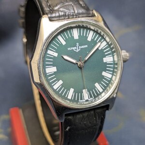 May include: A silver-toned Ulysse Nardin wristwatch with a dark green face and white markers. The watch has a black leather band. The watch face features the brand name and an anchor symbol. The watch is displayed on a black and red stand.